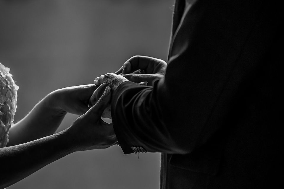 Black and white close-up photo of hands exchanging rings during an intimate wedding ceremony moment.