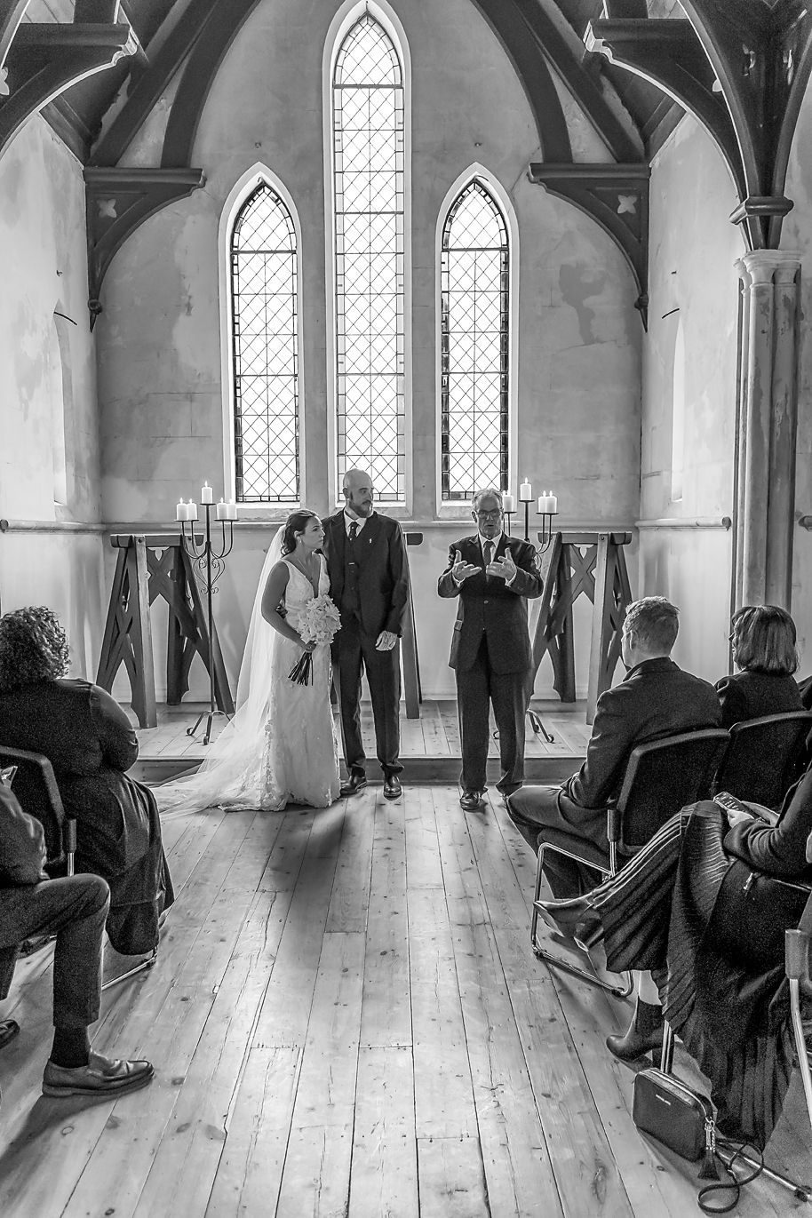 A wedding ceremony in progress inside a historic church with gothic arched windows and wooden floors.