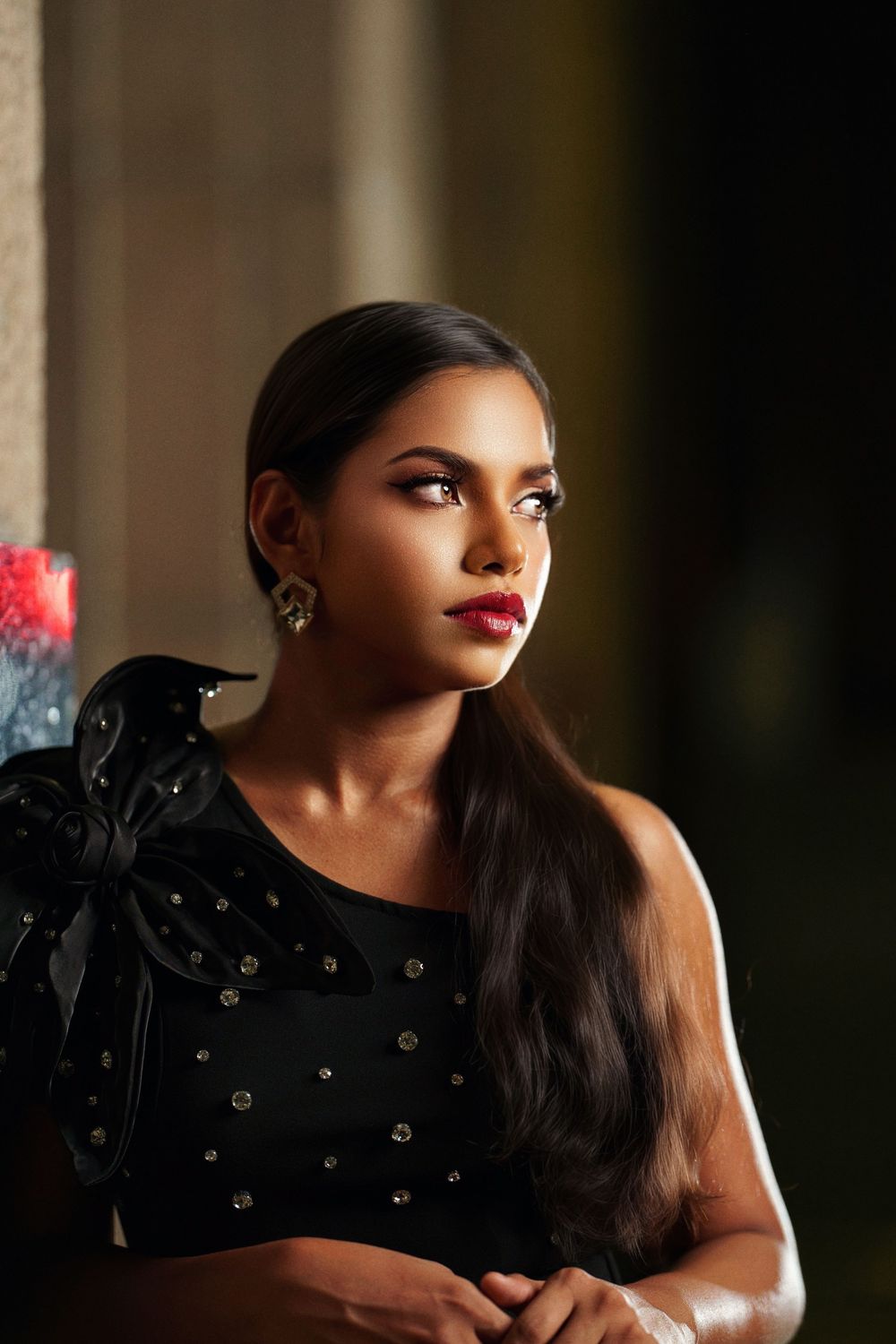A dramatic portrait featuring someone in a black embellished dress with bold red lipstick against a dark background.