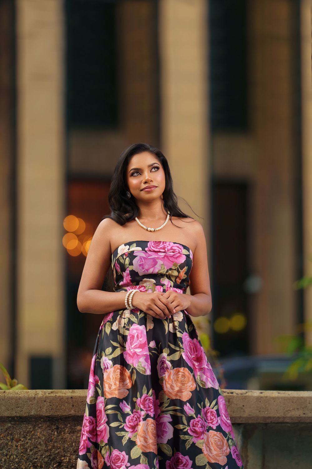 A floral print dress with pink and peach roses on black fabric is showcased in an outdoor portrait session.