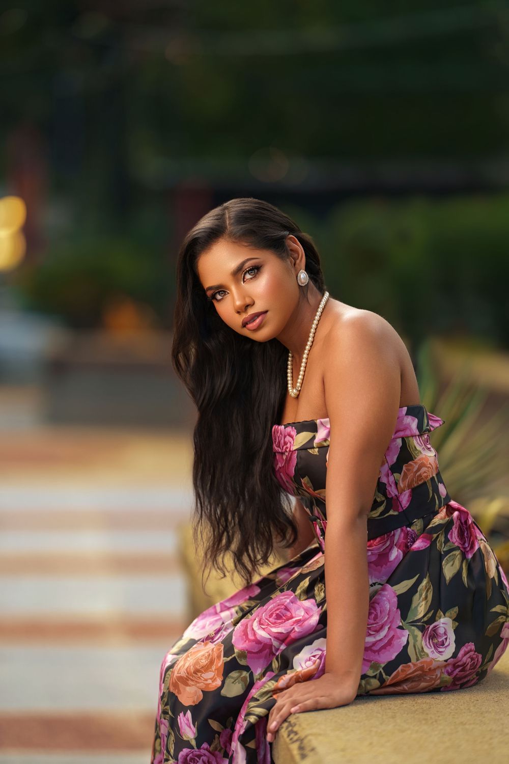 A woman in a floral dress poses gracefully on the ground during a golden hour photoshoot.