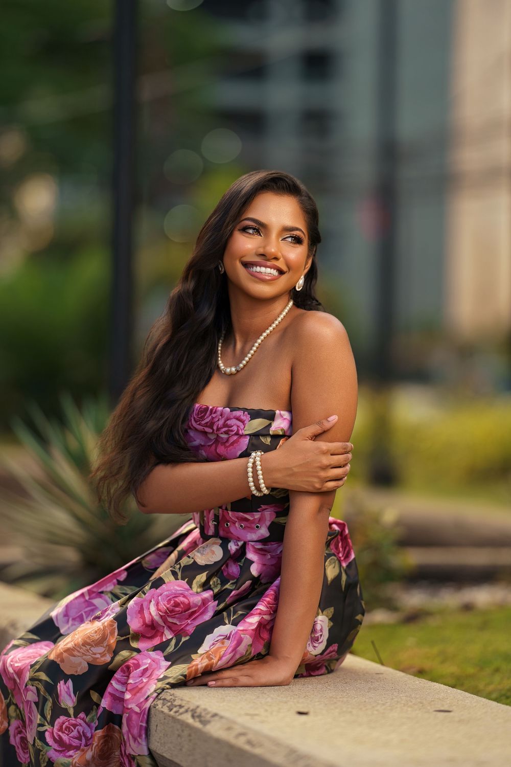 A stunning floral dress with pink roses is modeled outdoors against a soft-focus urban background.