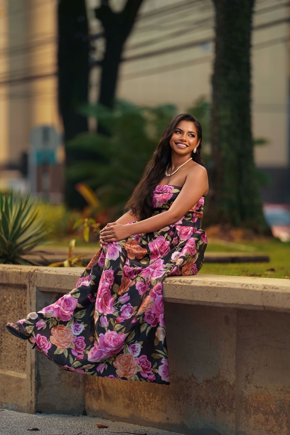 A floral dress flows elegantly as someone poses on a concrete ledge during golden hour.