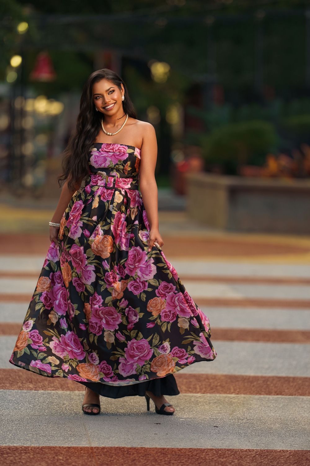 A flowing floral maxi dress is showcased in an evening outdoor photoshoot with bokeh lights.