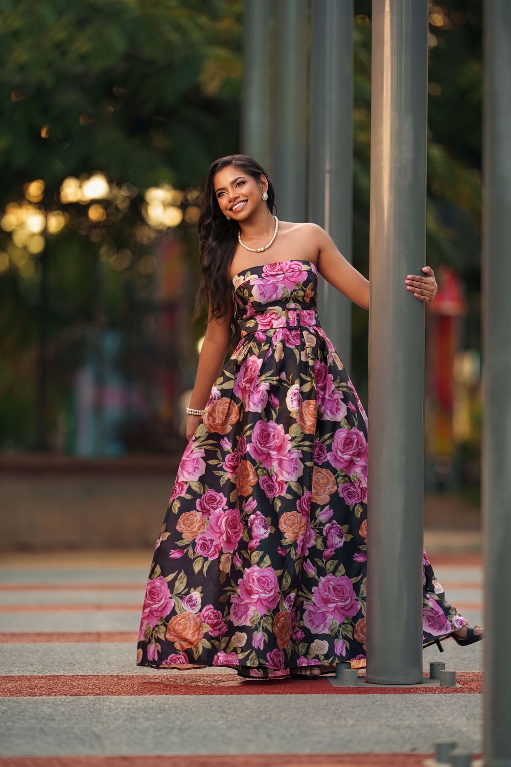 A vibrant pink and black floral dress stands out against an urban backdrop with columns and sunset lighting.