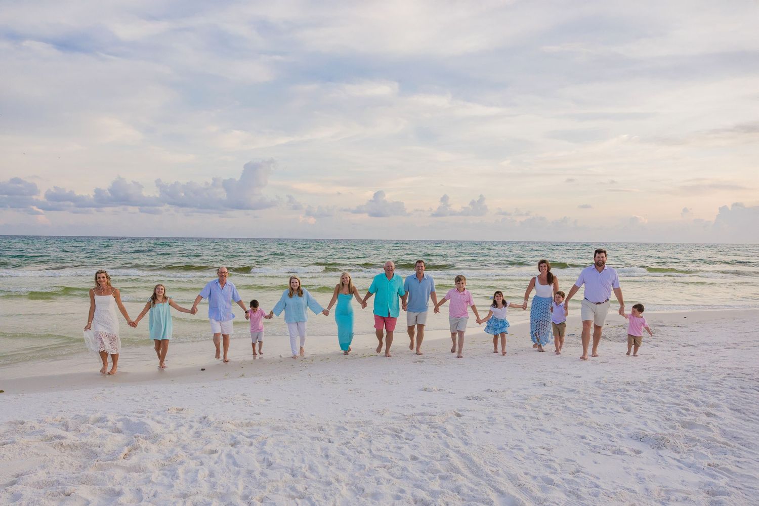 A group of people holding hands while walking along a white sandy beach at sunset with turquoise ocean waves.