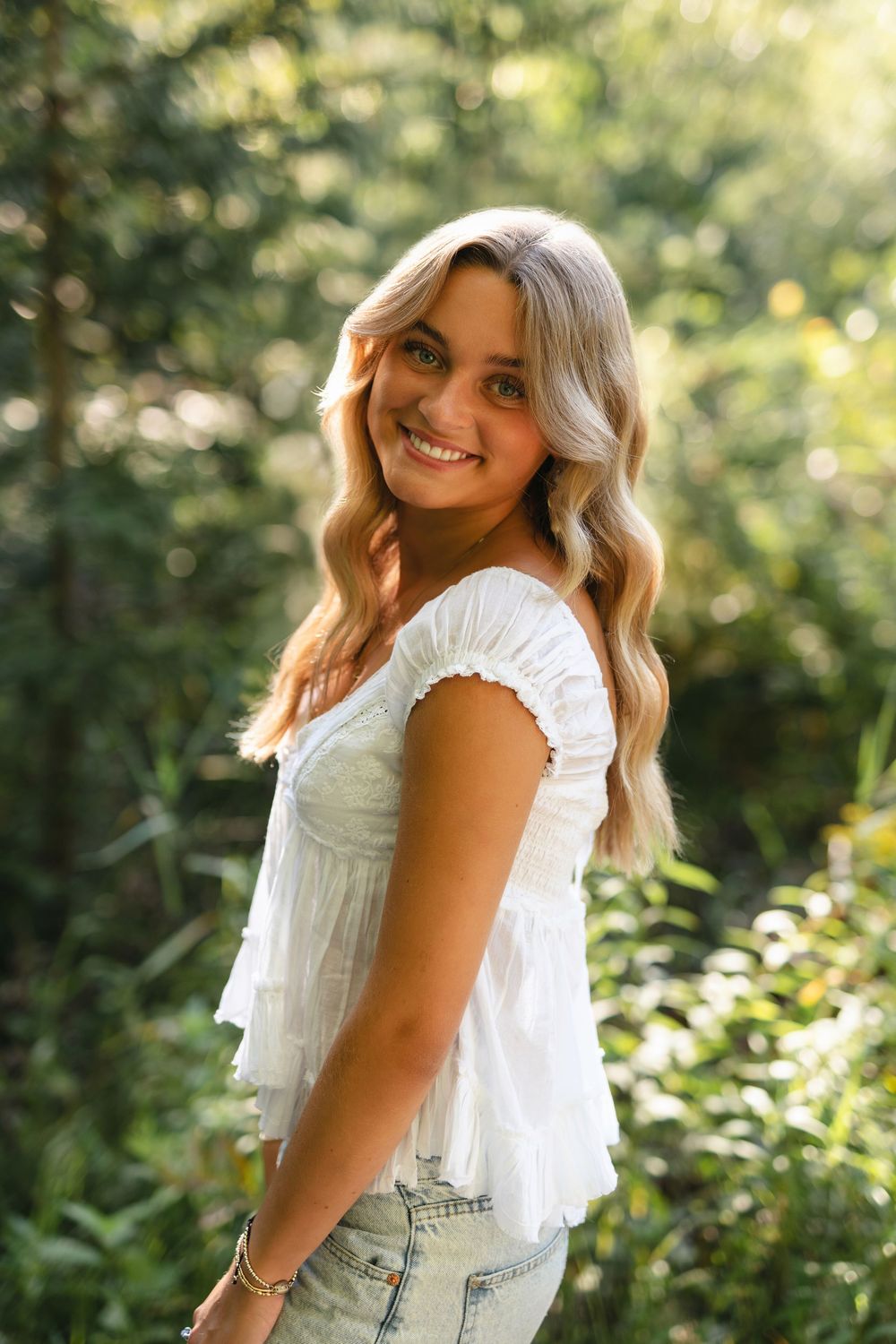 Casual summer portraits with ruffled white top and denim overalls in a sunlit garden with yellow flowers.