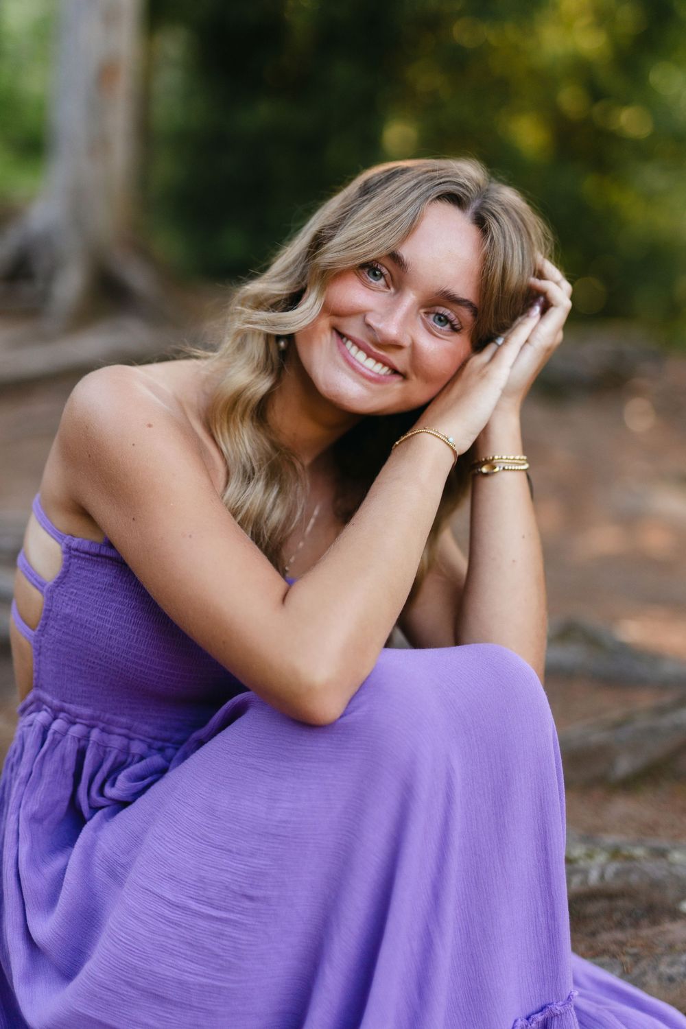 A person wearing a purple dress sits outdoors in natural lighting among trees.