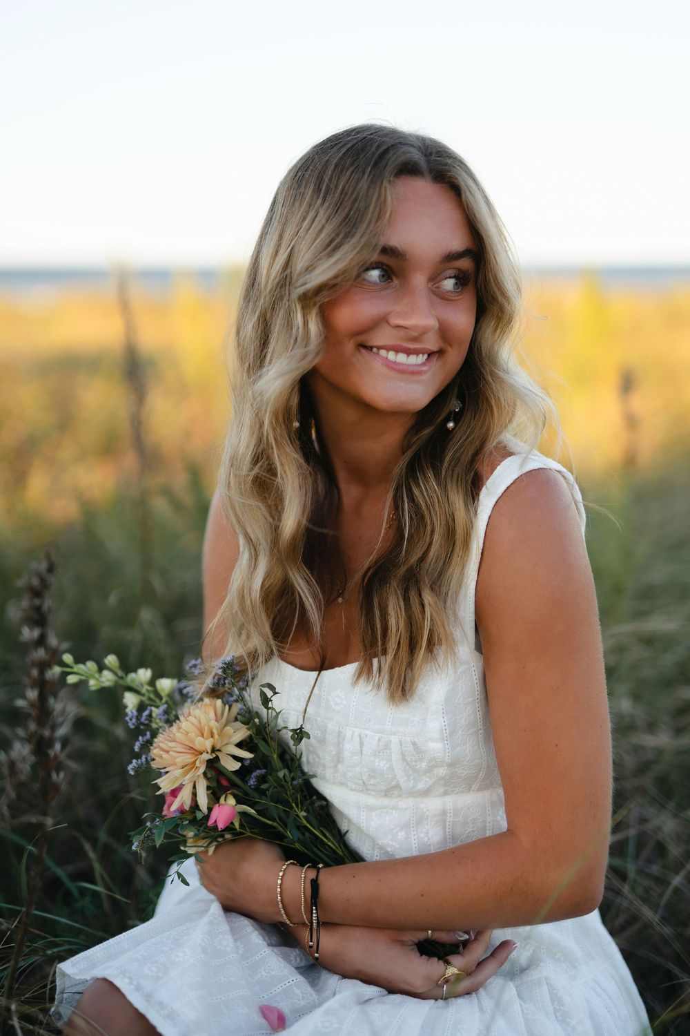 A white summer dress complements wildflowers in a golden field at sunset.