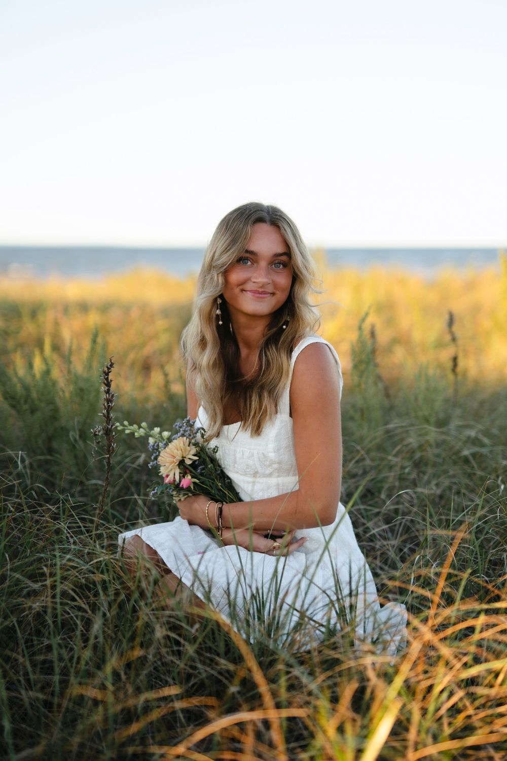 A person in a white dress sits in a golden field at sunset, creating a dreamy outdoor portrait series.