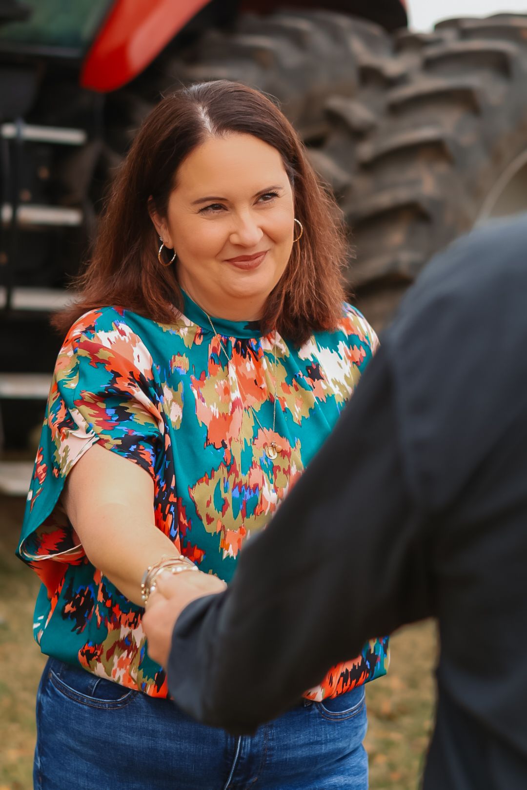 A portrait session featuring a vibrant teal and orange floral top against a farm backdrop.