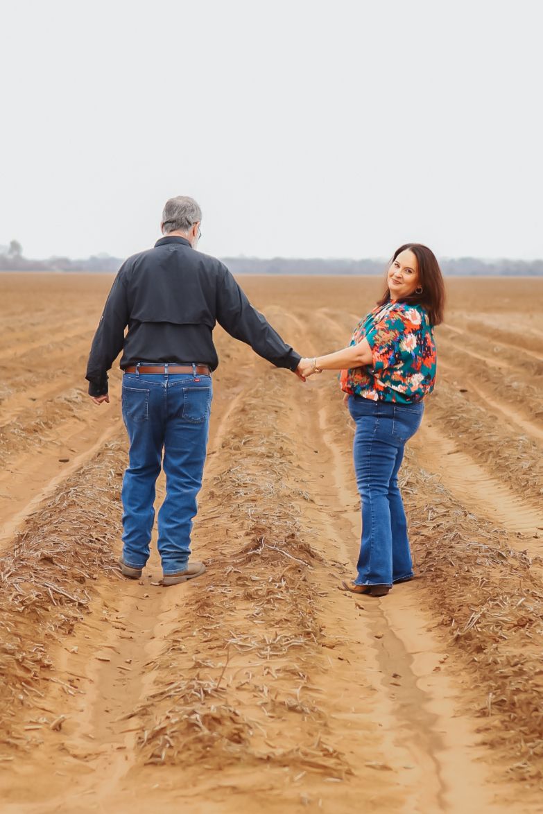 Two people walking together through plowed farm fields on a cloudy day.