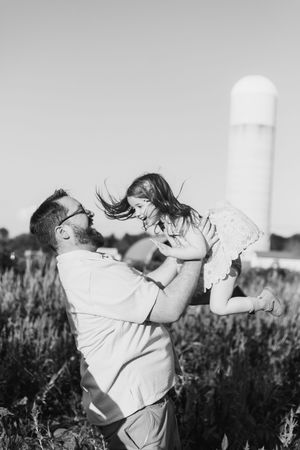 Black and white photo of a tender moment between parent and child playing in a field with a water tower in background.