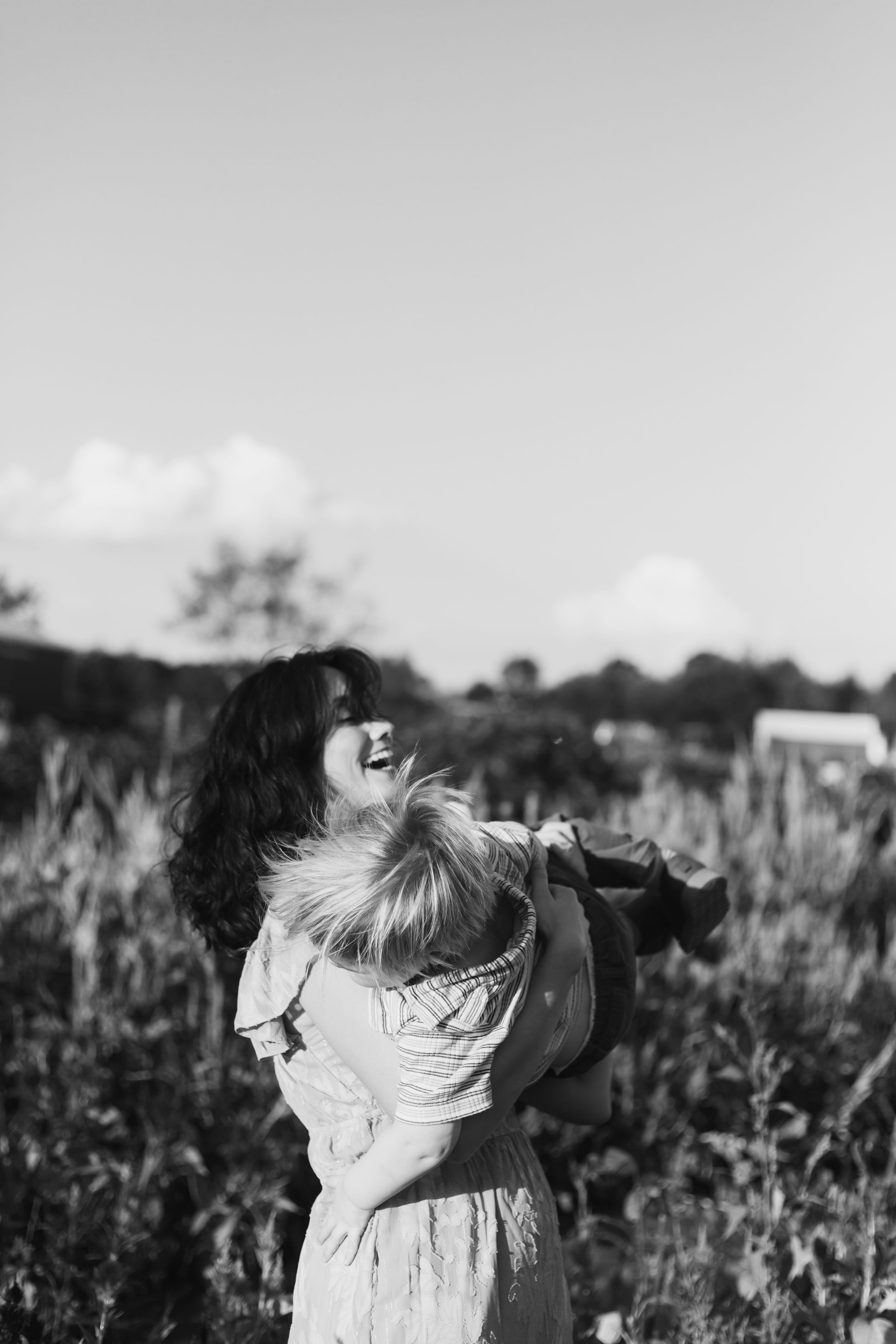 Two children in white dresses play together in a sunlit meadow filled with wildflowers in black and white.