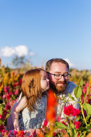 Two people share an intimate moment among red and yellow wildflowers under blue skies.