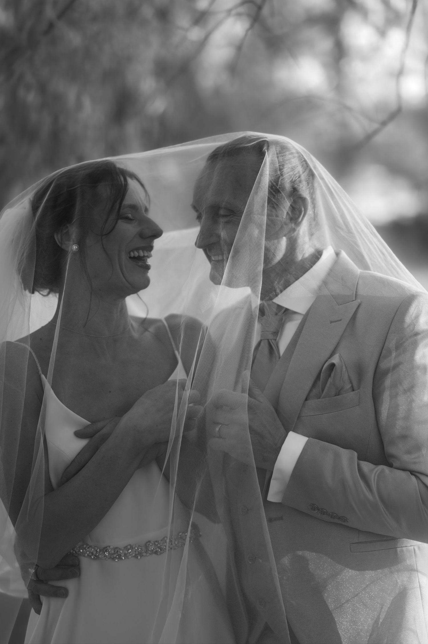 Une photo de mariage en noir et blanc montrant un moment joyeux partagé sous un voile de mariée.