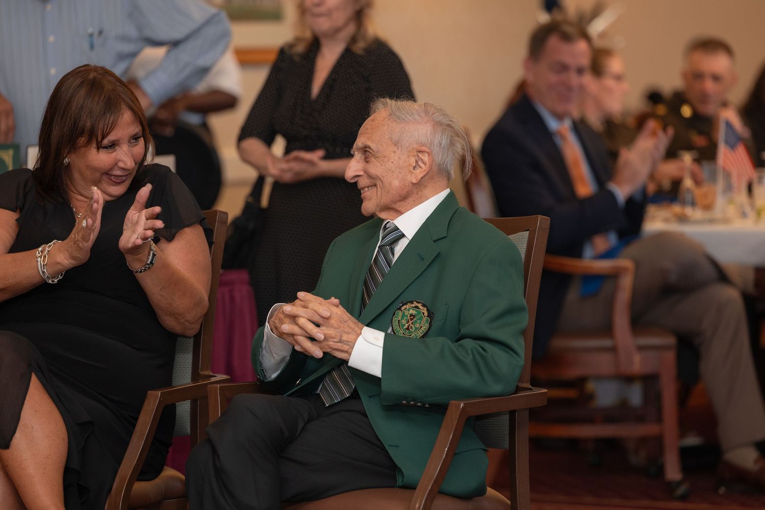 Elegant dining room celebration with attendees in formal attire and green blazers.