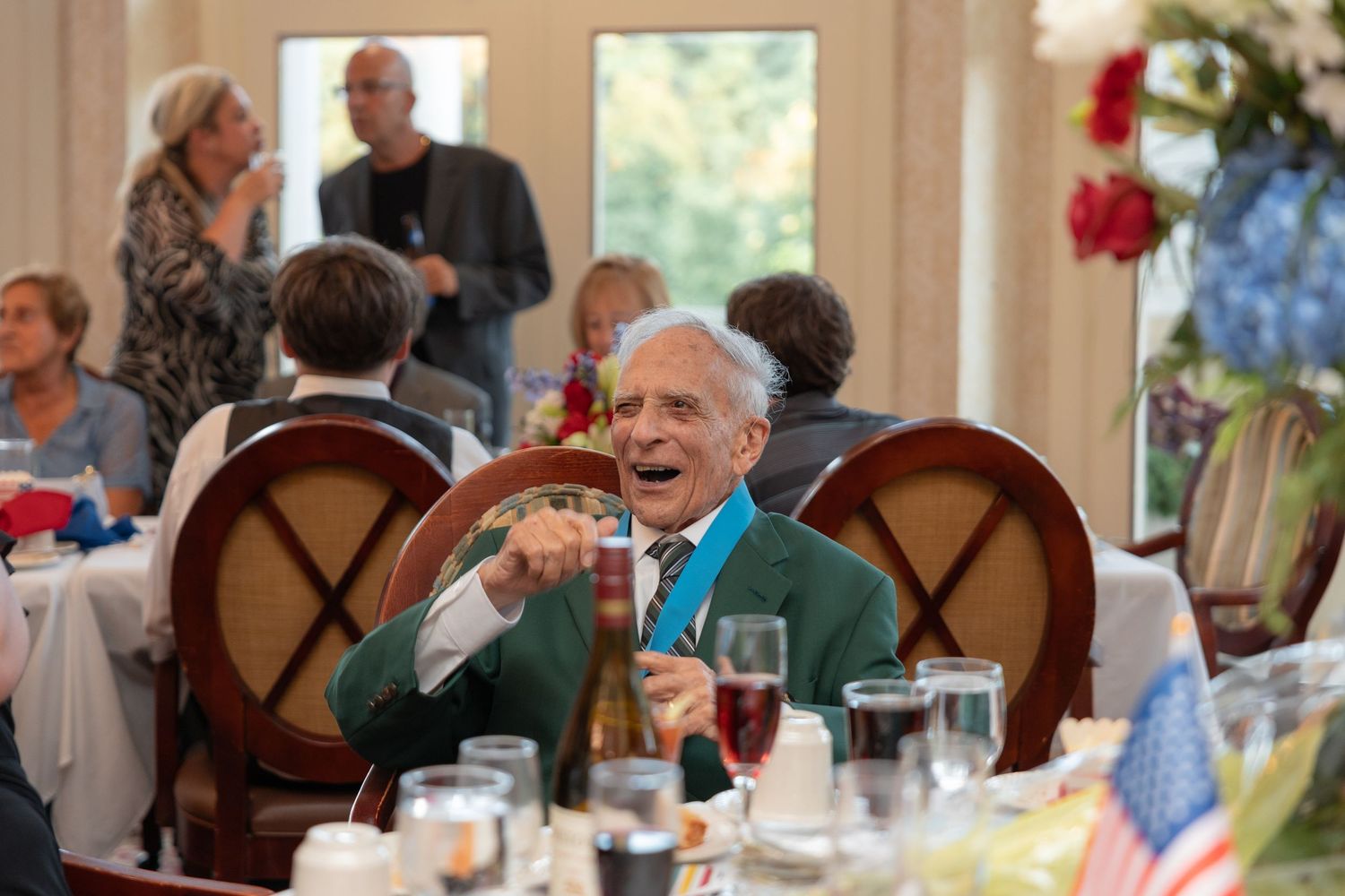 Person in green jacket laughs heartily while seated at decorated dining table during special event.