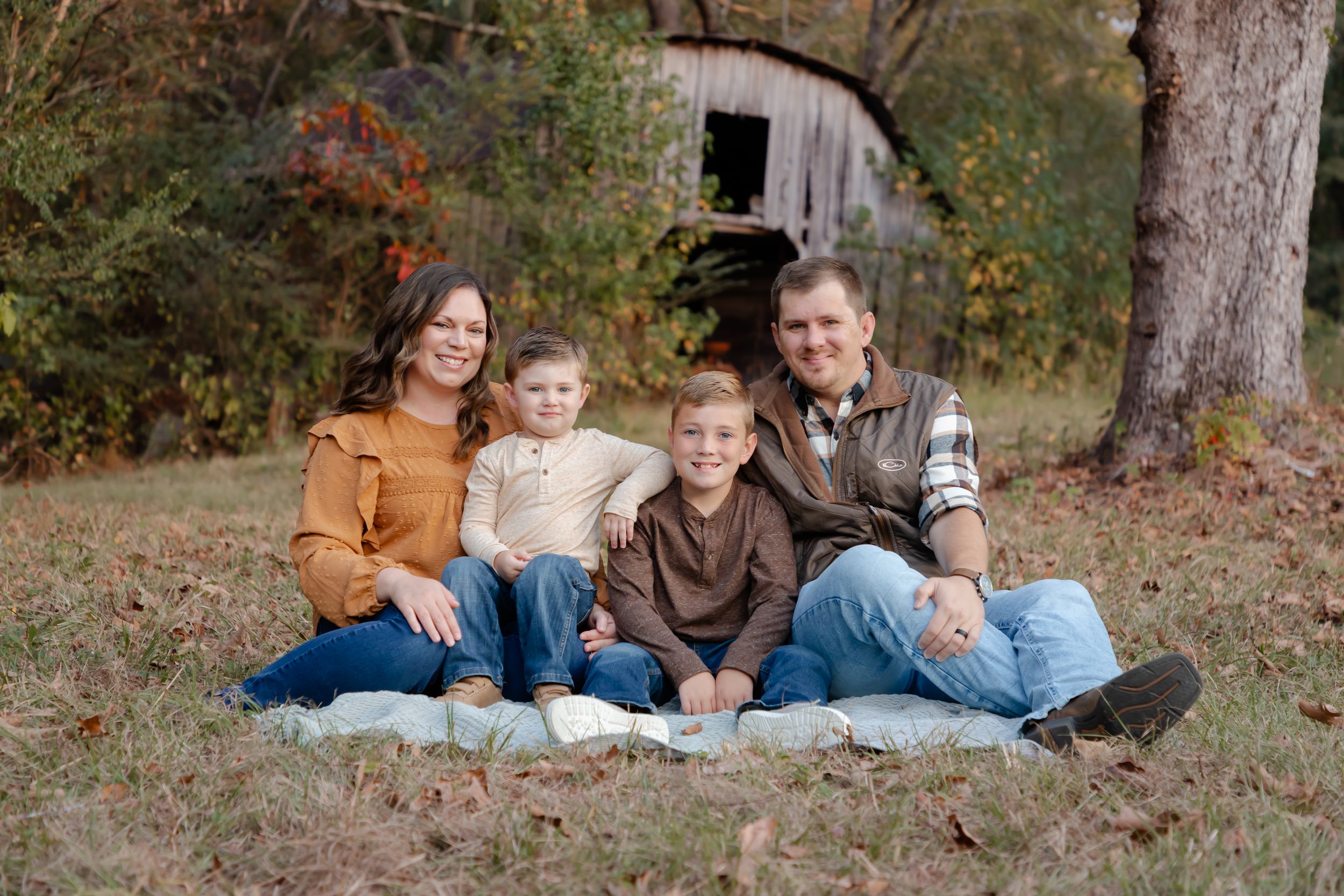 Family group sitting together on autumn ground surrounded by trees and fallen leaves.