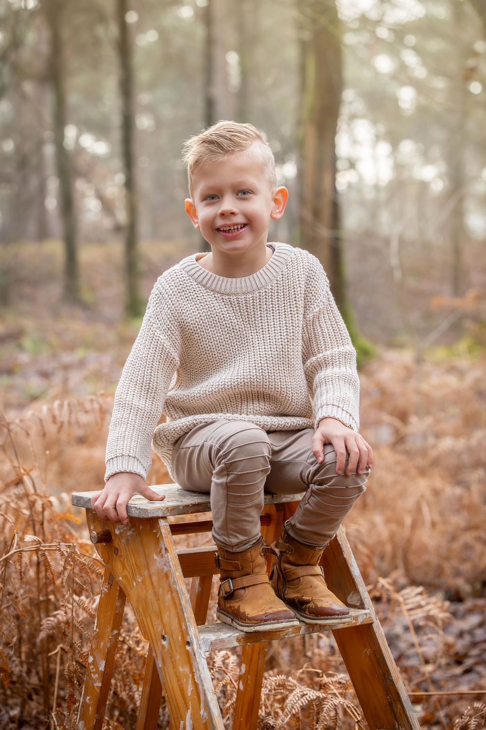 vrolijk lachend kind op houten schildertrap. gekleed in bruin en creme kleuren. ommen