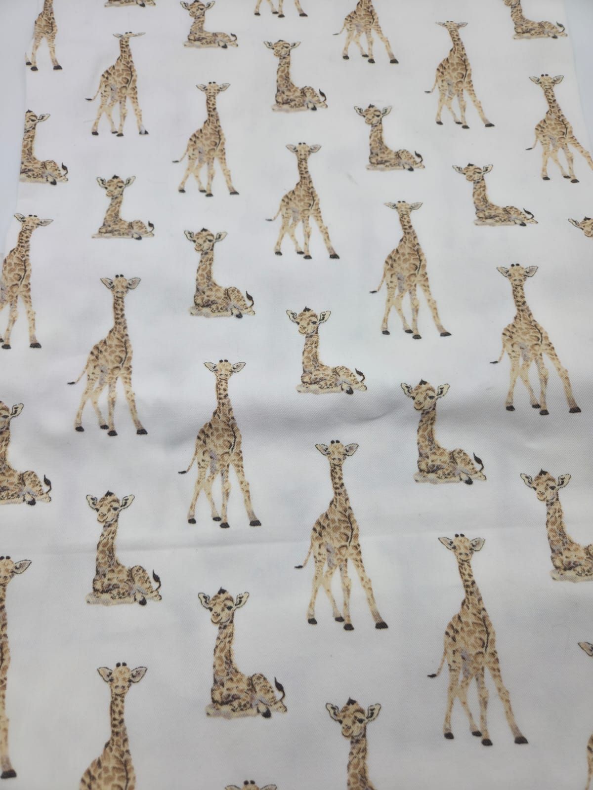 Repeating pattern of small beige giraffe silhouettes on light gray fabric background.
