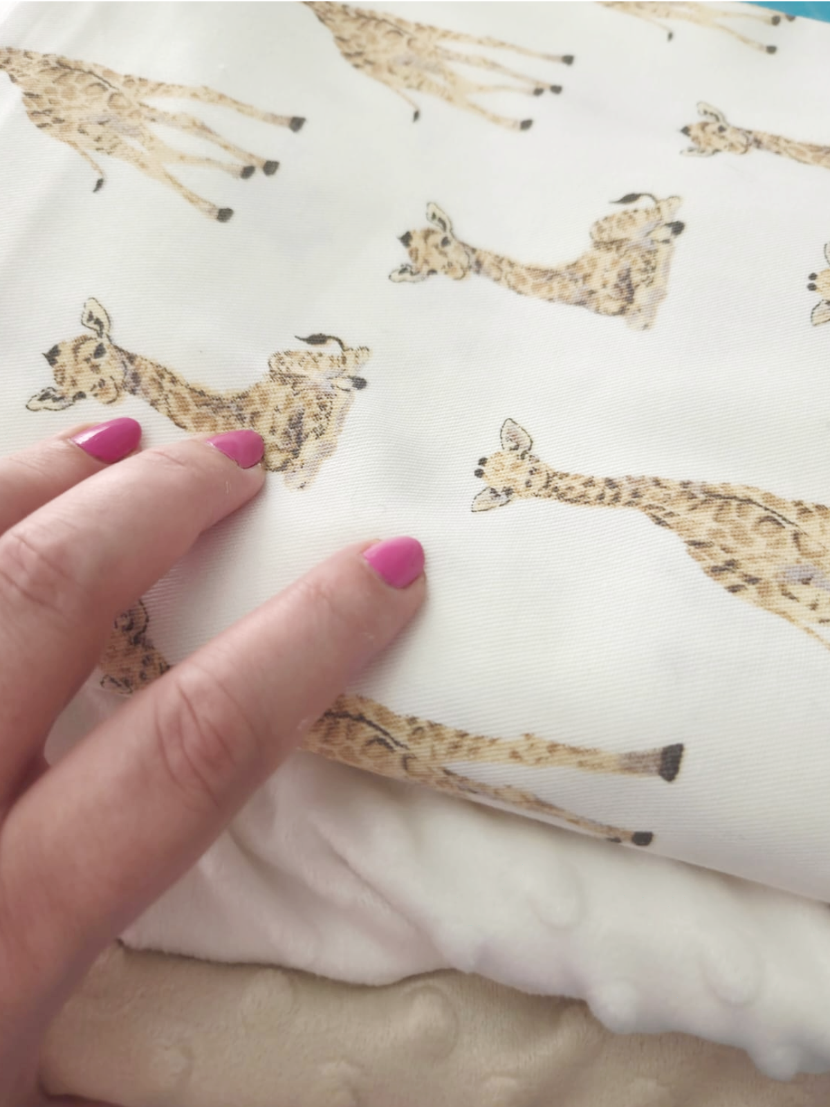 A hand with pink nail polish presses down on a white and beige patterned fabric with repeating giraffe designs.