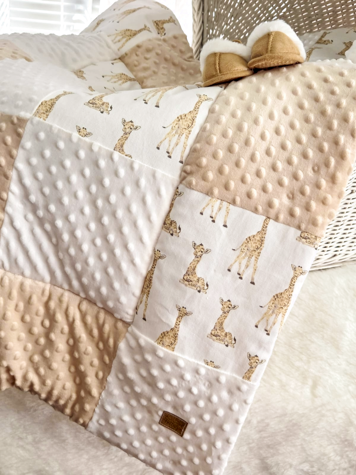 Close-up of a baby blanket with giraffe print pattern and minky dot texture in neutral beige and white tones.