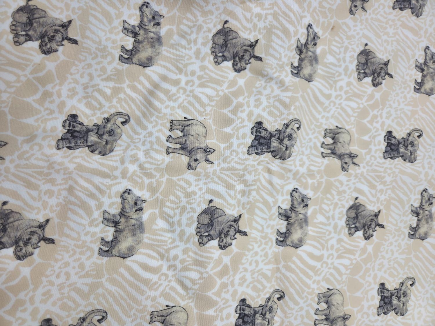 Repeating pattern of small gray elephants and butterflies printed on light beige textured fabric.
