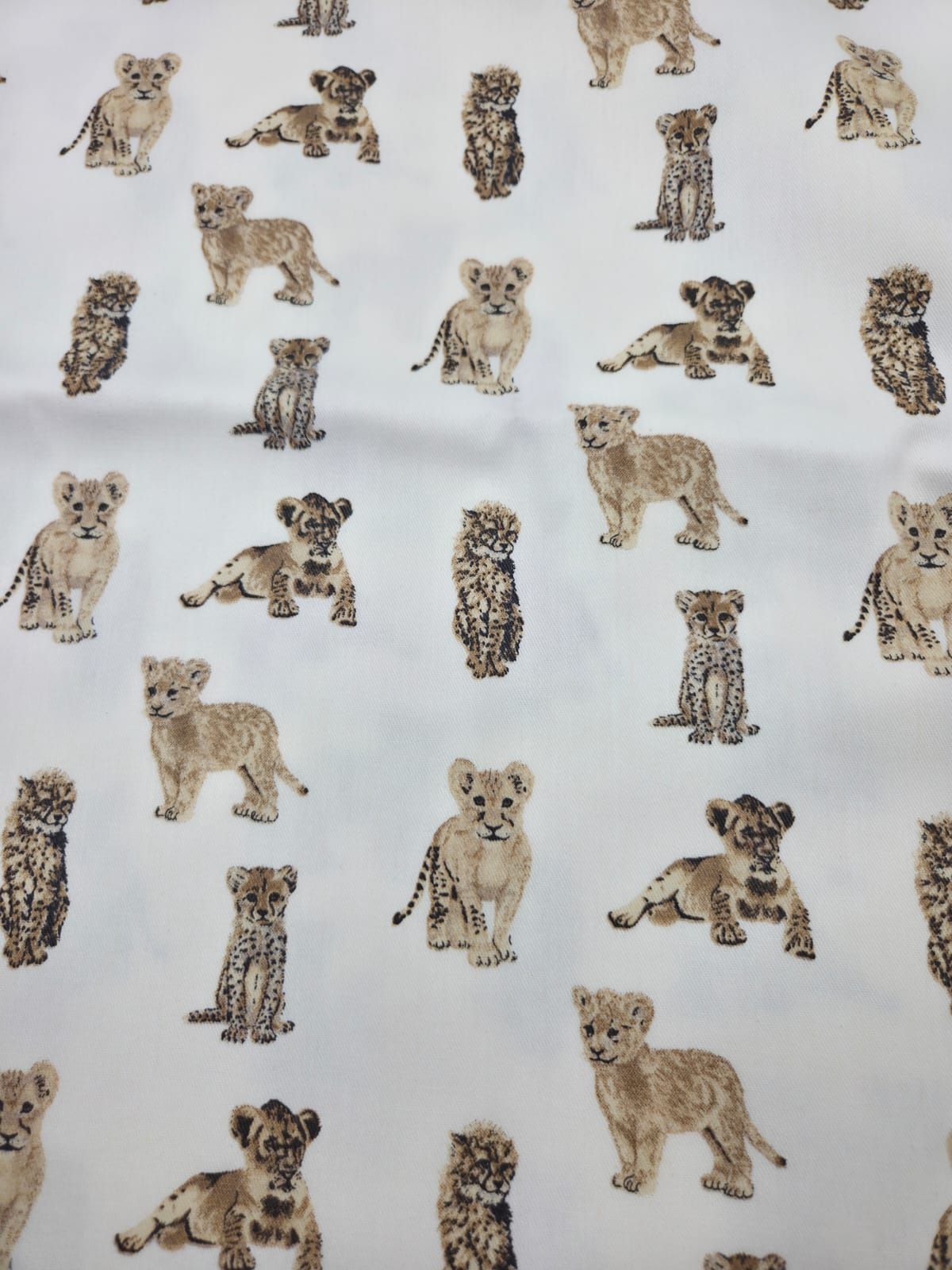 Repeating pattern of baby lion cubs, cheetahs and leopards on white fabric creating a cute safari animal design.