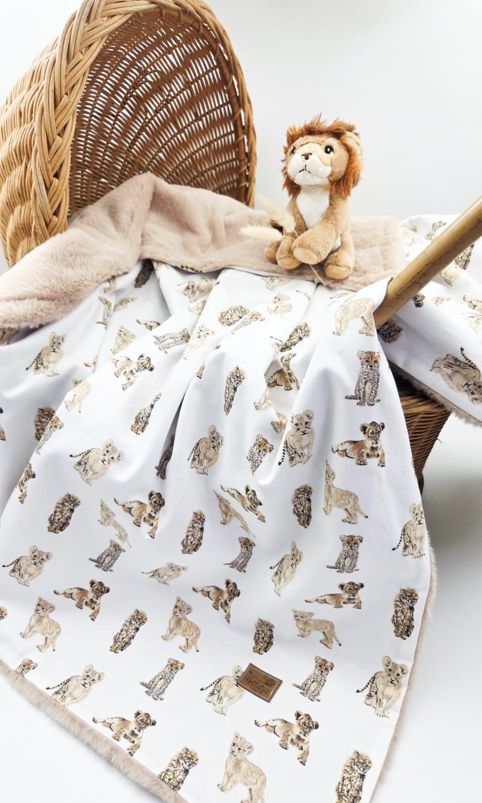 White baby blanket with beige puppy print pattern shown draped over wicker basket display.