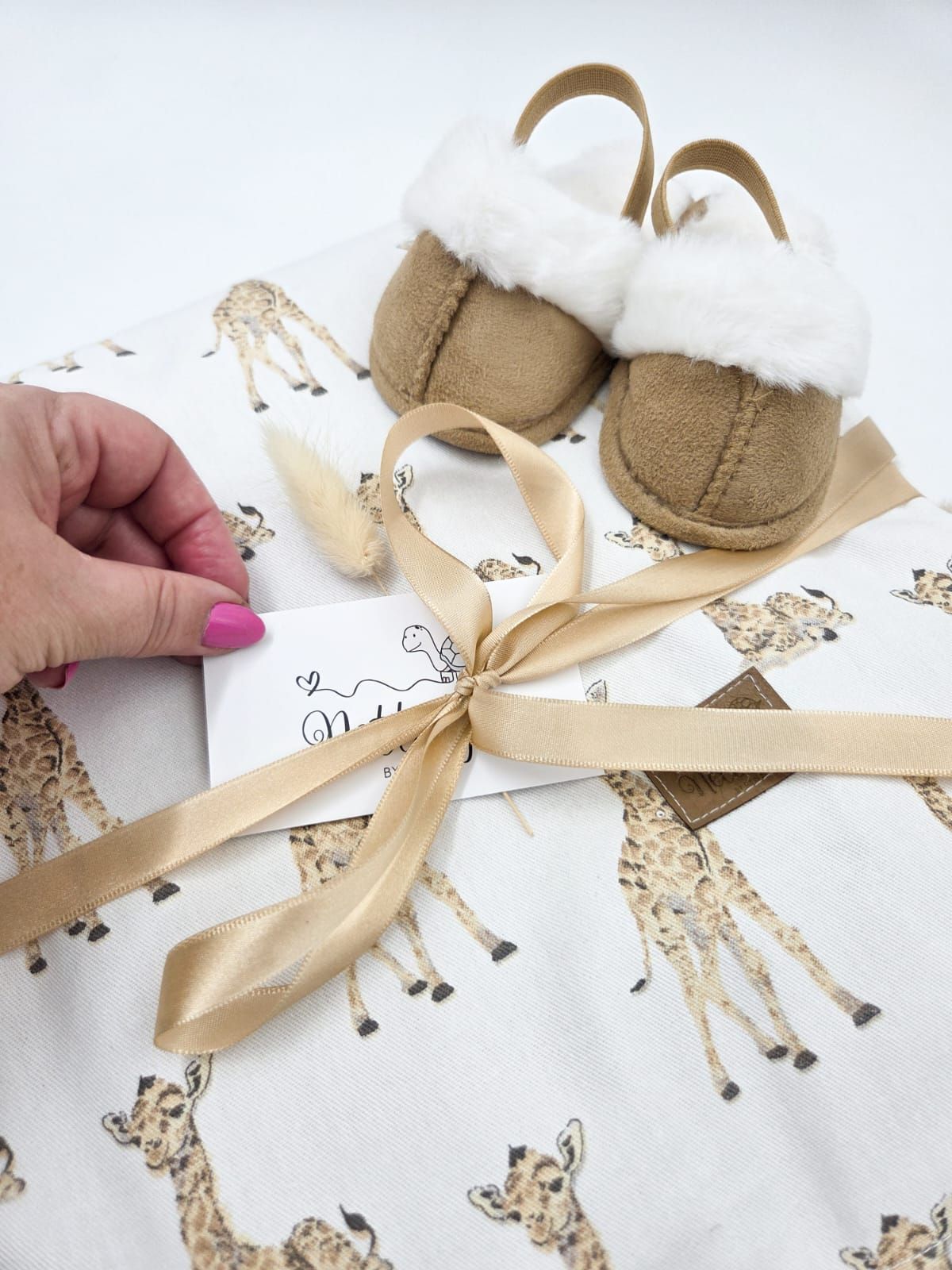 A series of hands tying a beige ribbon bow on a soft plush baby bootie with animal print fabric.