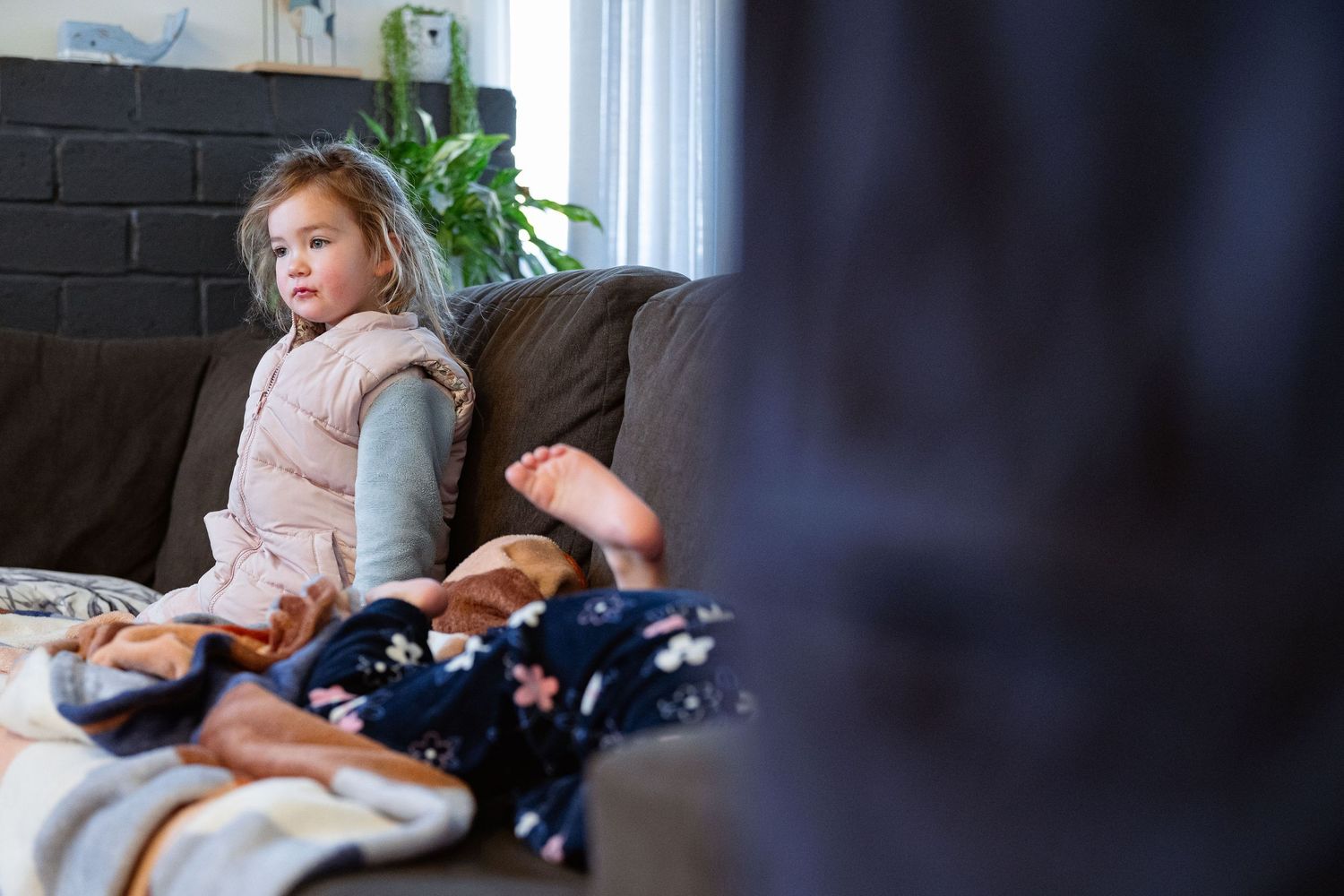 A baby sleeps peacefully on a couch while sunlight streams through nearby windows.