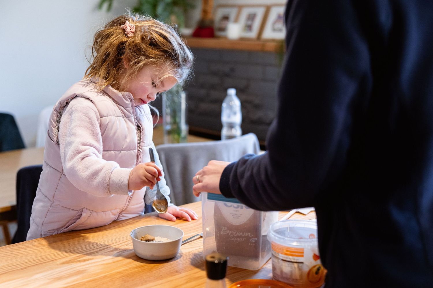 A child uses a small brush to paint or draw at a wooden table with art supplies.