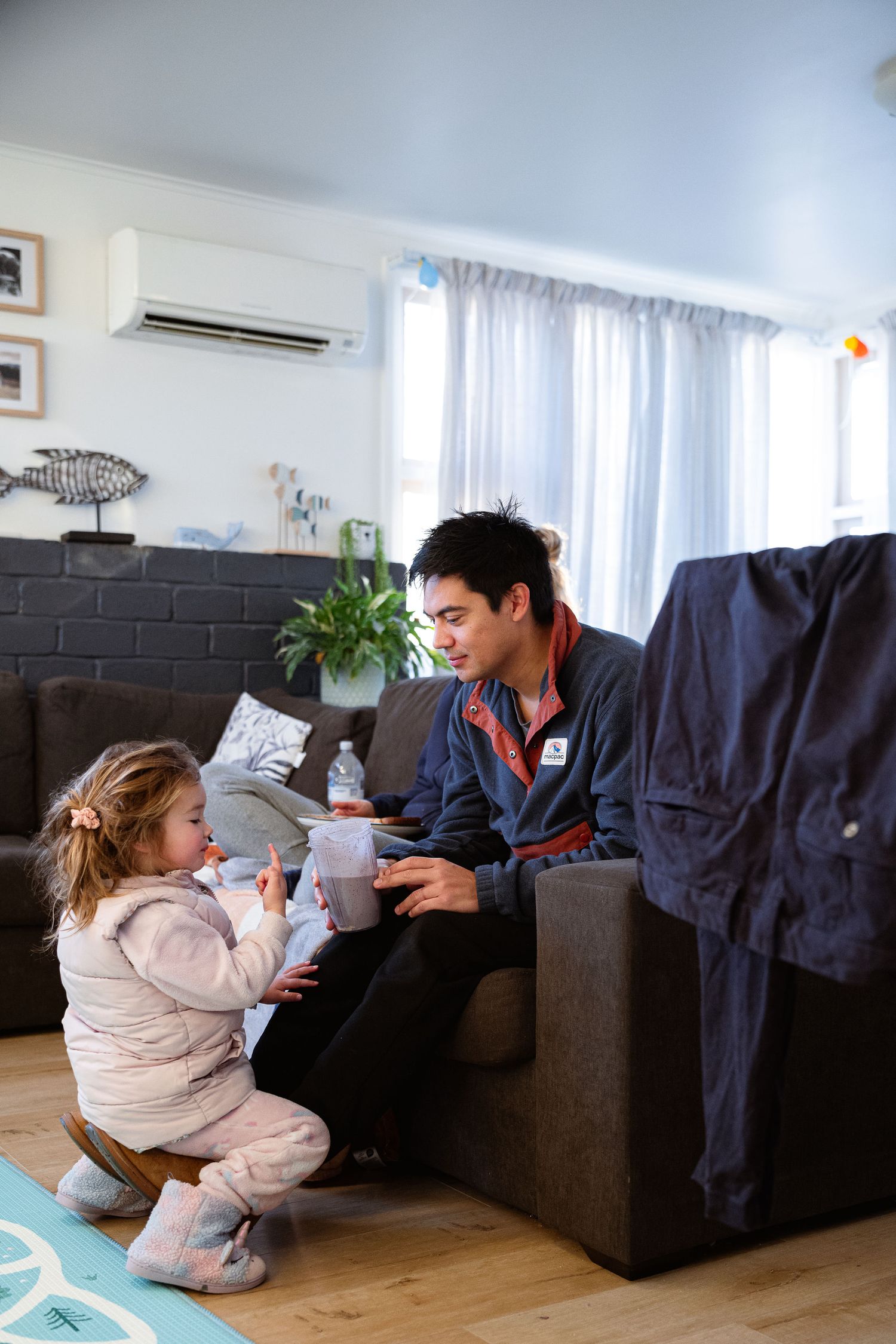 Two people playing and interacting together on a couch in a bright modern living room with hardwood floors.
