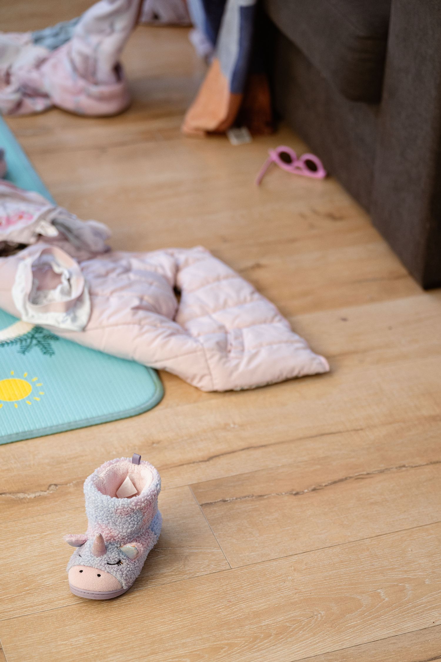 Small pink baby shoes and socks arranged on light wooden flooring with a turquoise mat visible.