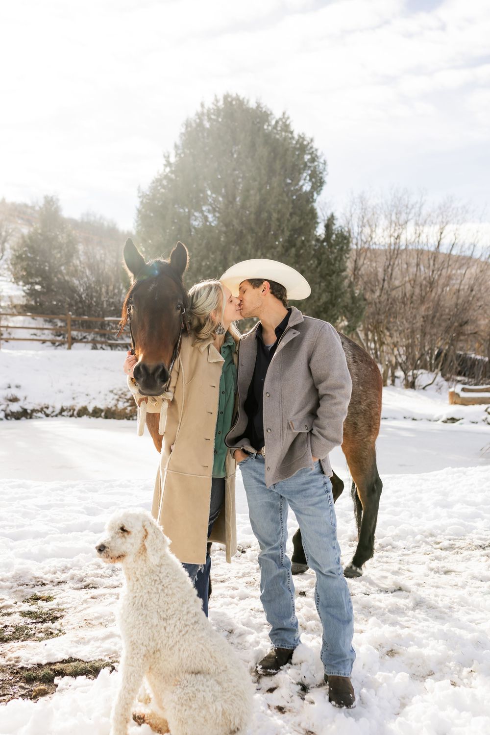 couple kissing beside a horse and dog during a winter couples photo session in Utah