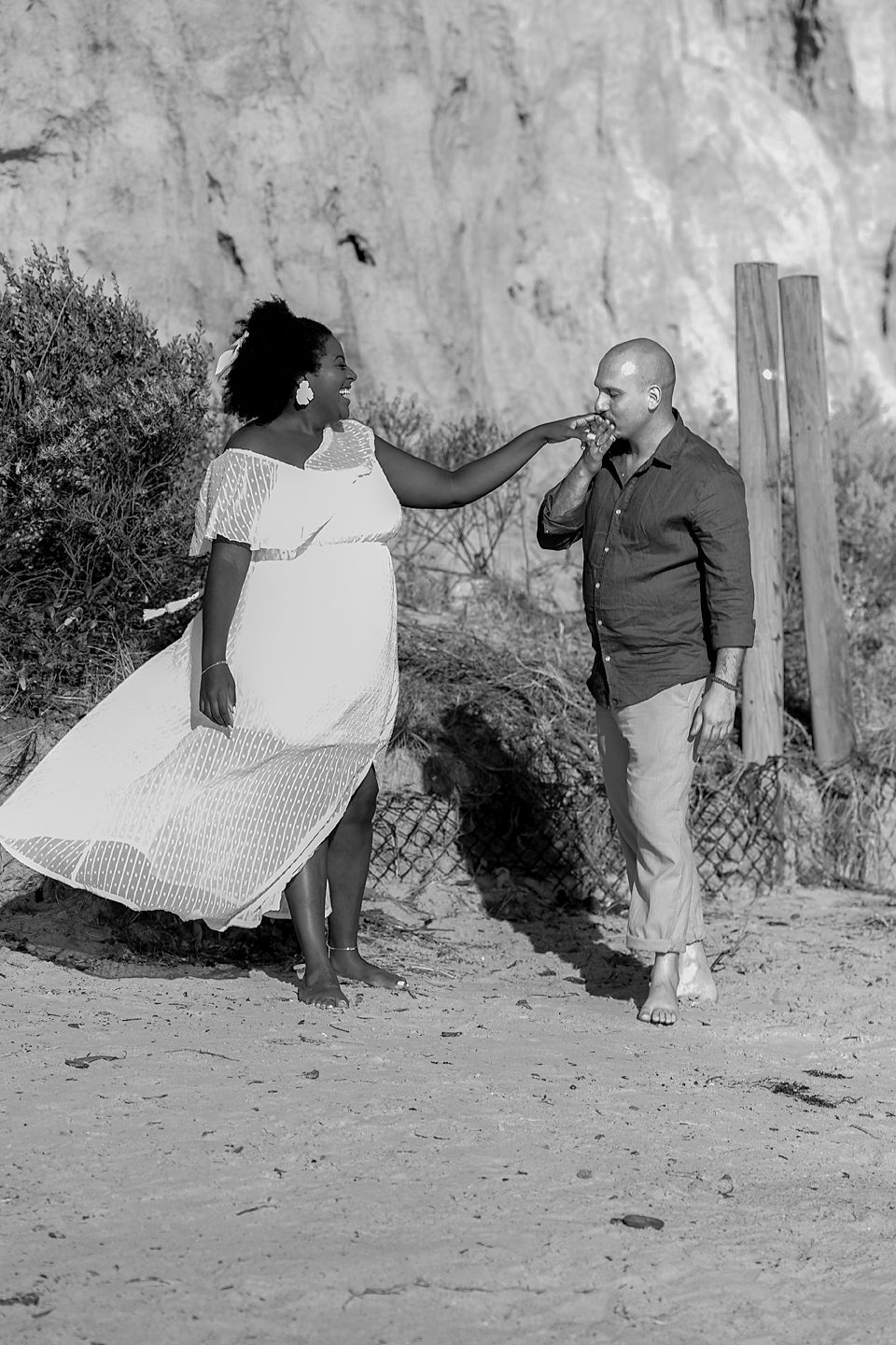 A sequence of black and white photos showing two figures playfully interacting on a sandy beach near a rock wall.