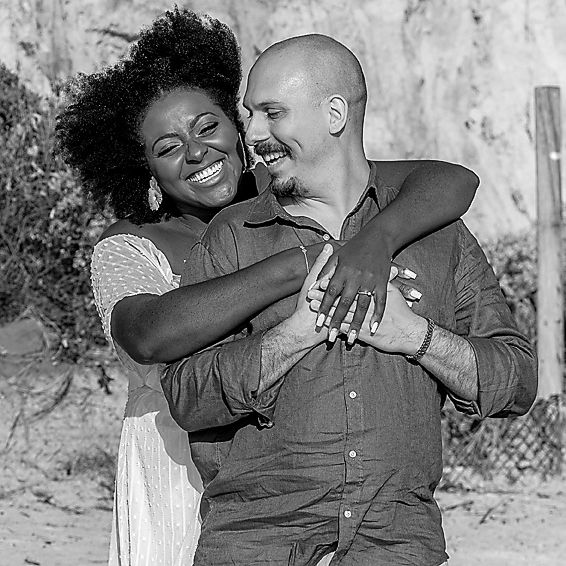 A couple embraces and shares joyful laughter while posing against a textured wall in black and white photography.
