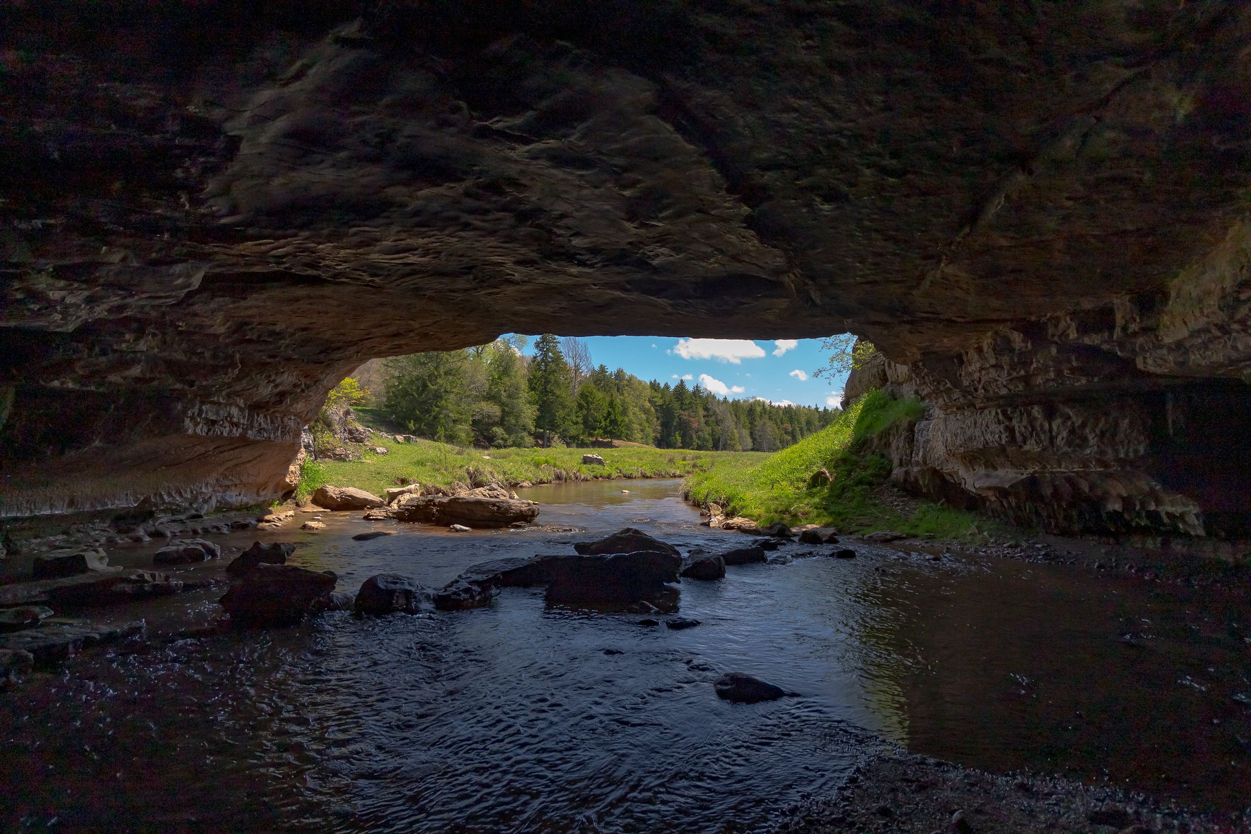 Natural rock cave opening overlooking a serene water body with sunlight streaming in.