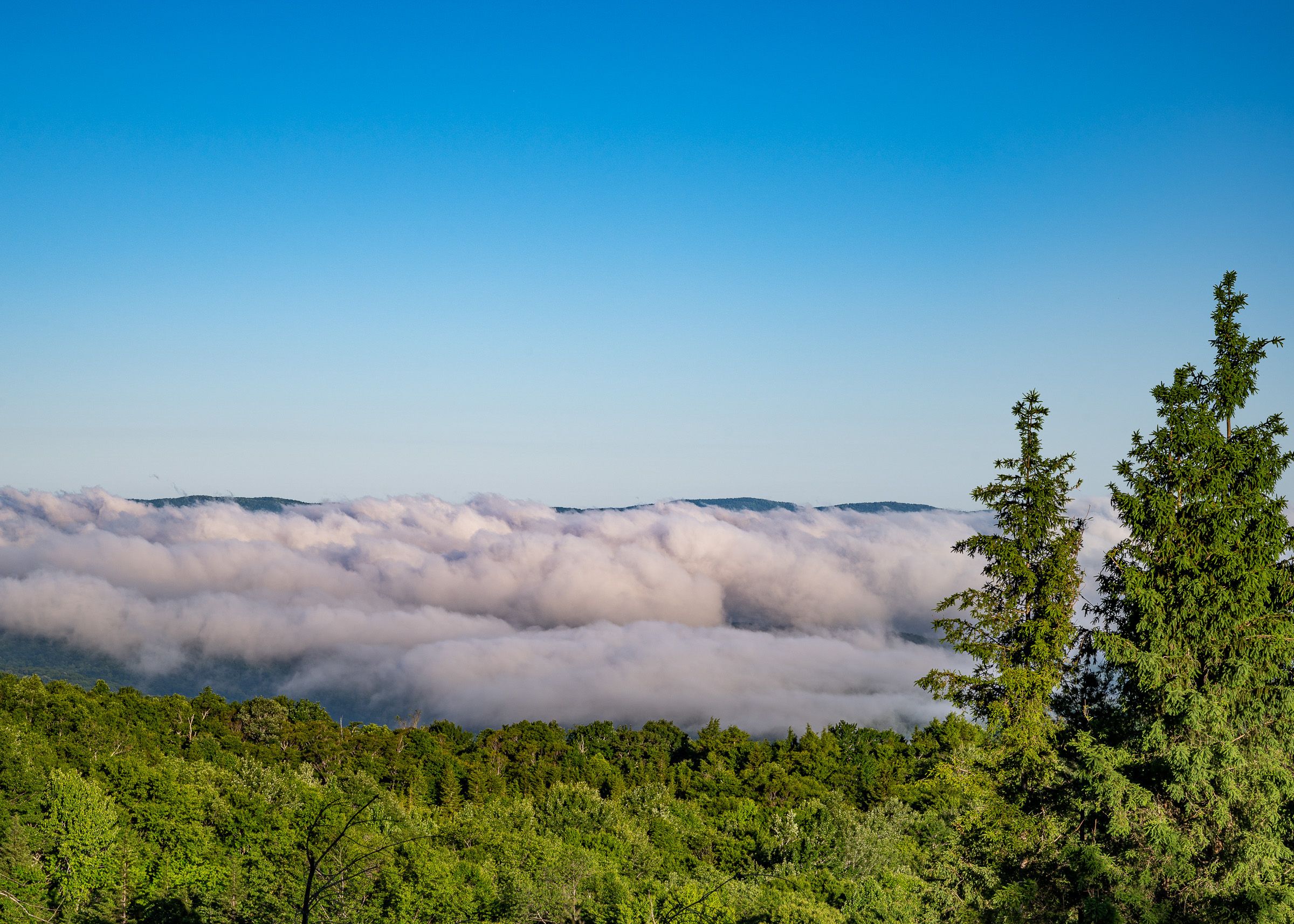 Rolling mountains fade into the distance under a bright blue sky with low-lying clouds.