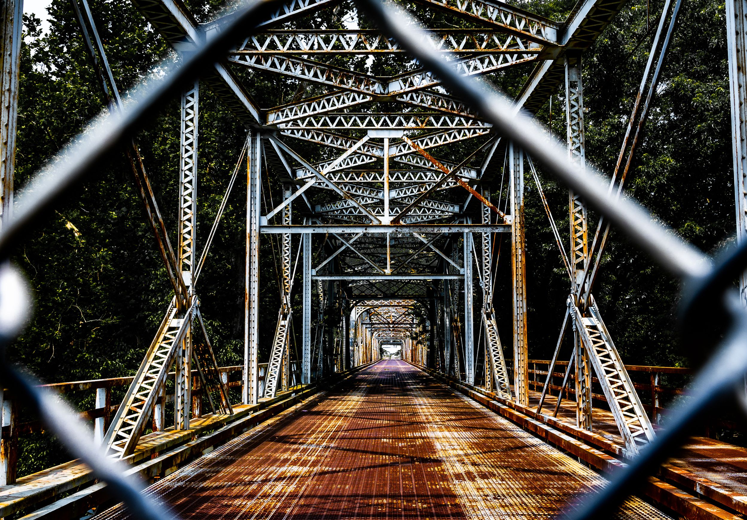 Metal truss bridge stretches across a river creating a dramatic perspective view.