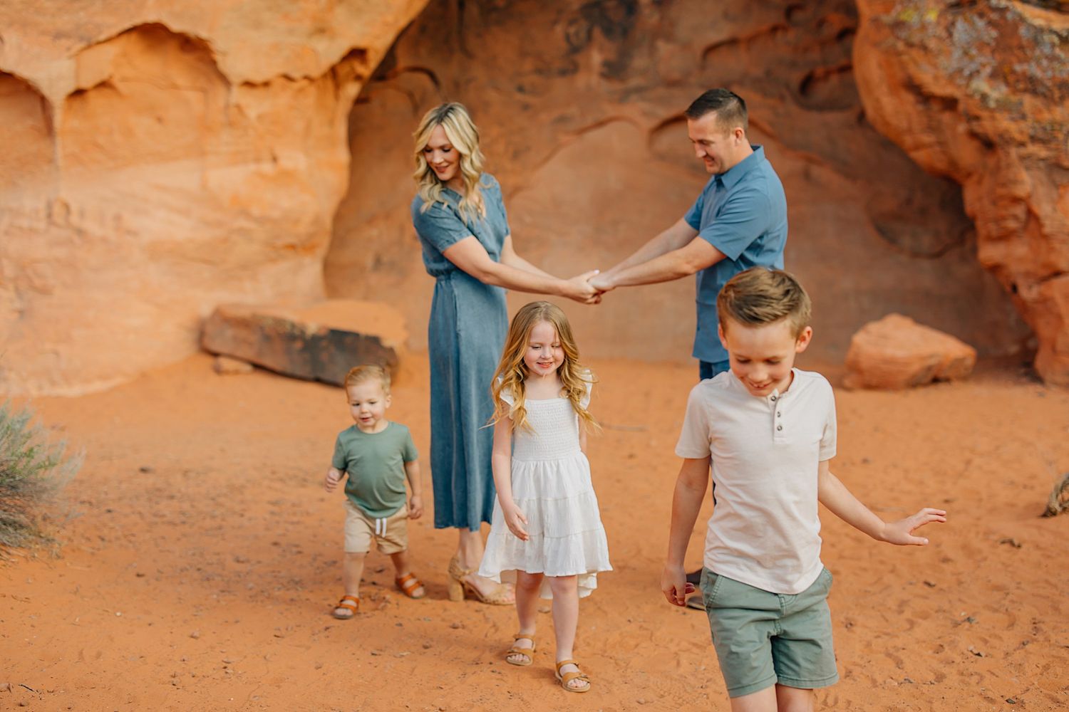 A couple explores vibrant red rock formations in a desert landscape during golden hour.