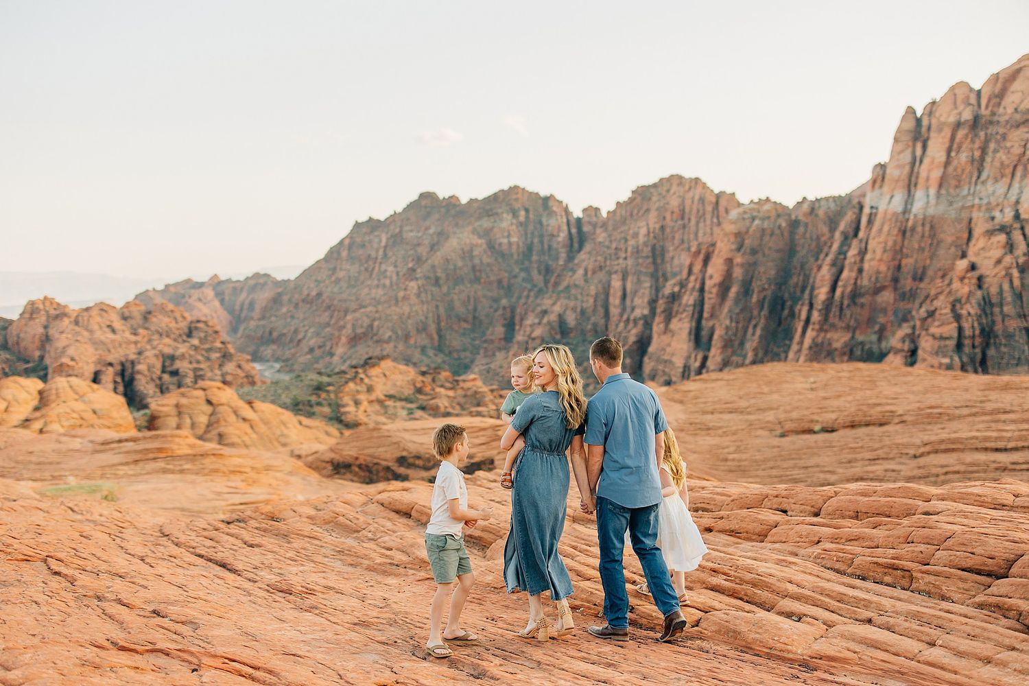 Family enjoying scenic views together on red rock formations at Snow Canyon State Park in Utah during sunset.