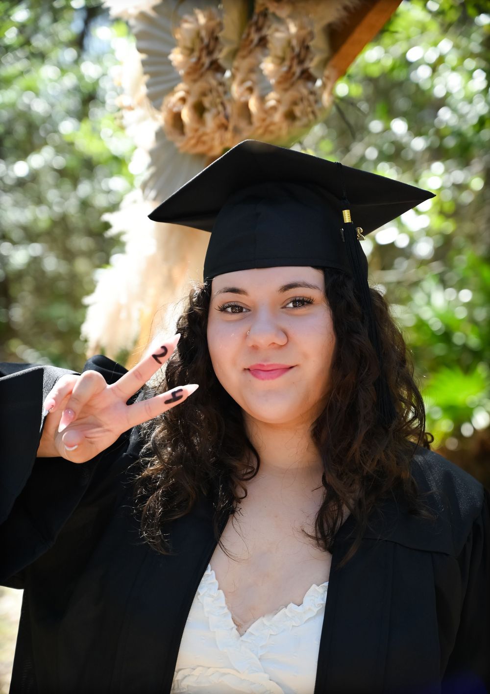 Graduate in black cap and gown and white lace dress poses outdoors with joyful expressions during graduation photoshoot.