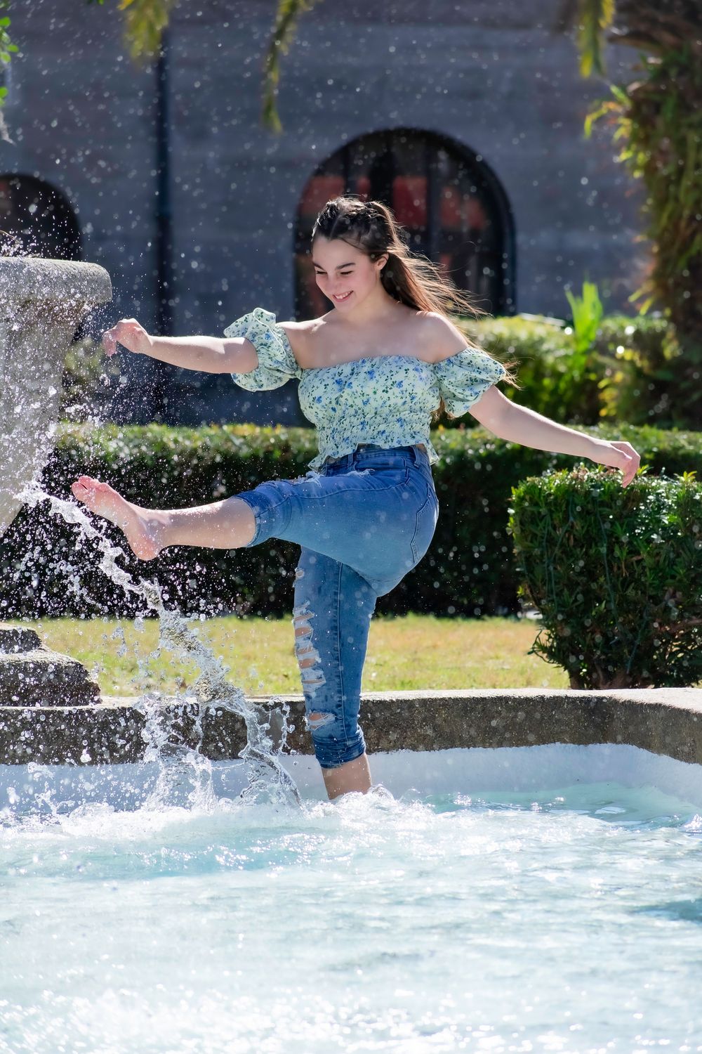 Person in denim shorts and blue top splashing and playing in a pool on a sunny summer day.
