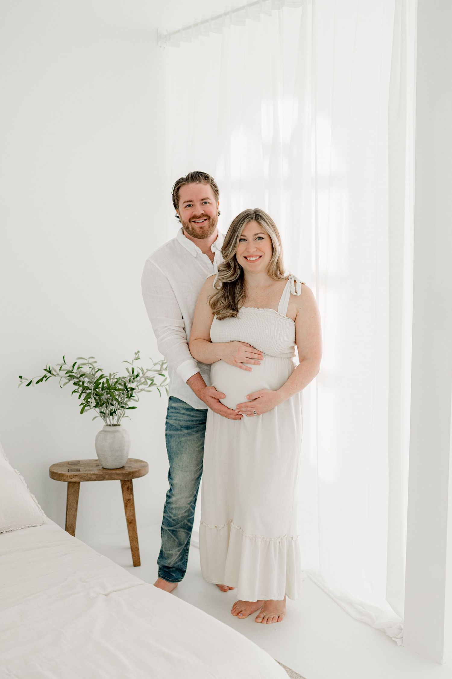 A couple in white studio with minimalist decor and natural lighting ​captured by ​​Ashley Wilson, maternity photographer in Jacksonville, FL