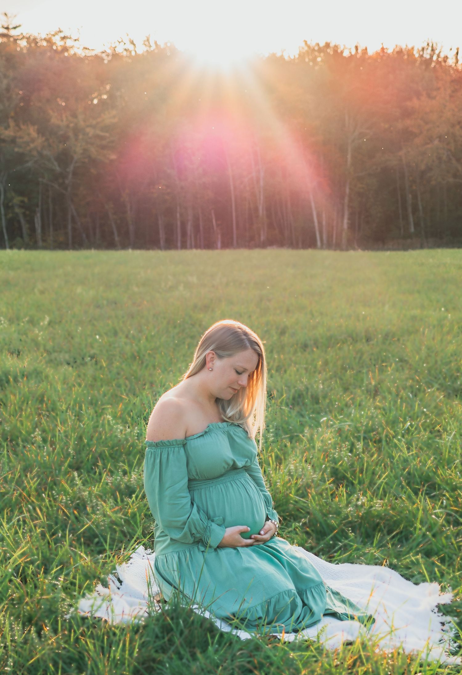A person in a turquoise dress sits in a sunlit meadow at sunset, creating a dreamy outdoor scene.