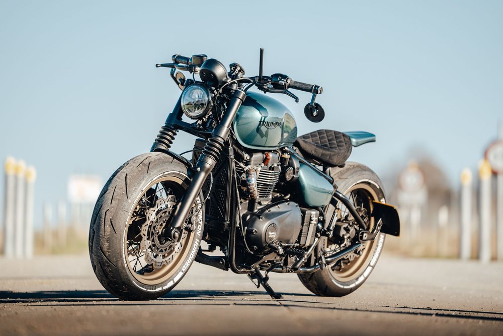 Custom blue motorcycle parked on asphalt with blurred background during sunset.