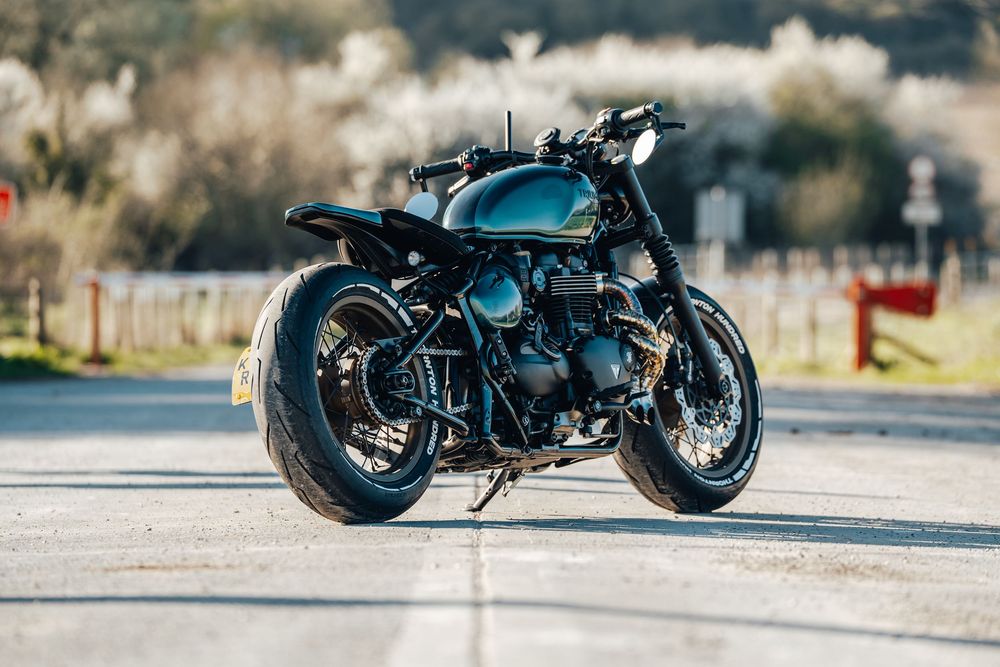 Custom black motorcycle photographed from side profile on an empty road with blurred background.