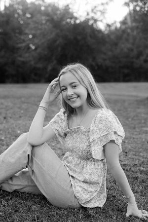 Black and white portrait series of someone lying in grass wearing a floral top and smiling joyfully.